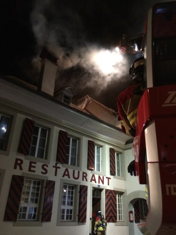 Starker Rauch auch im Bereich des Kamins; Feuerwehrmänner auf der Autodrehleiter zur Intervention bereit. 