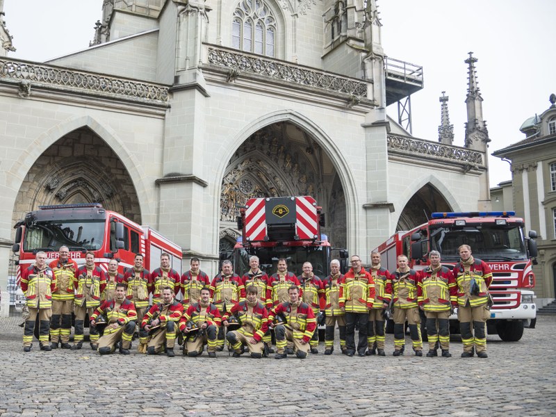 Die fünf neuen Berufsfeuerwehrmänner auf dem Münsterplatz, umgeben von ihren Kameraden. Im Hintergrund Einsatzfahrzeuge.