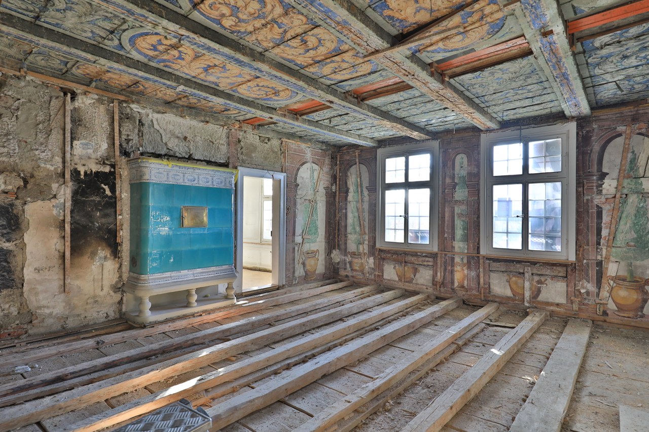 Sogenanntes Götterzimmer mit frühbarocken Wandmalereien, Kachelofen und Decke mit Rankenmalerei auf blauem Hintergrund. Bild: Hebeisen + Vatter Architekten, Bern.
