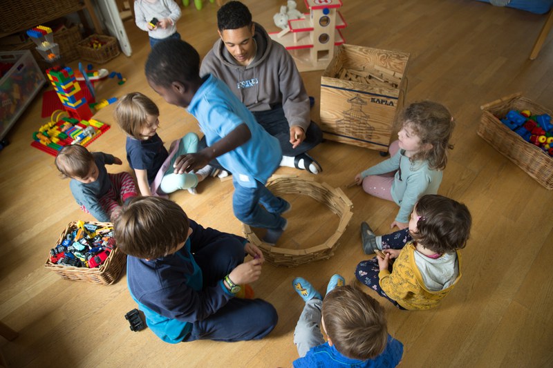 Kindergruppe und Betreuer spielen gemeinsam mit Holzbausteinen