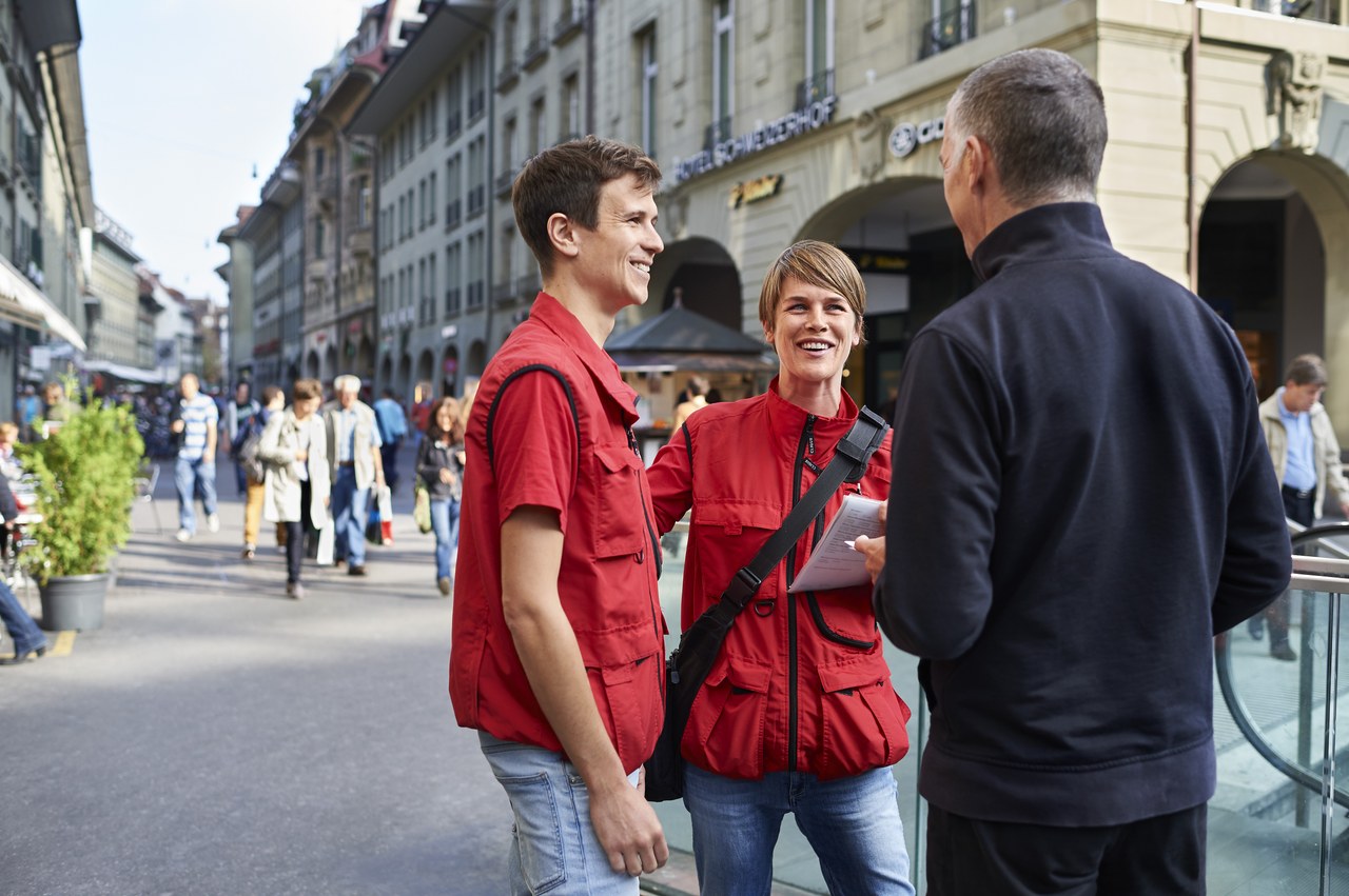 Eine Pinto-Mitarbeiterin und ein Pinto-Mitarbeiter im Gespräch mit einem Passanten.