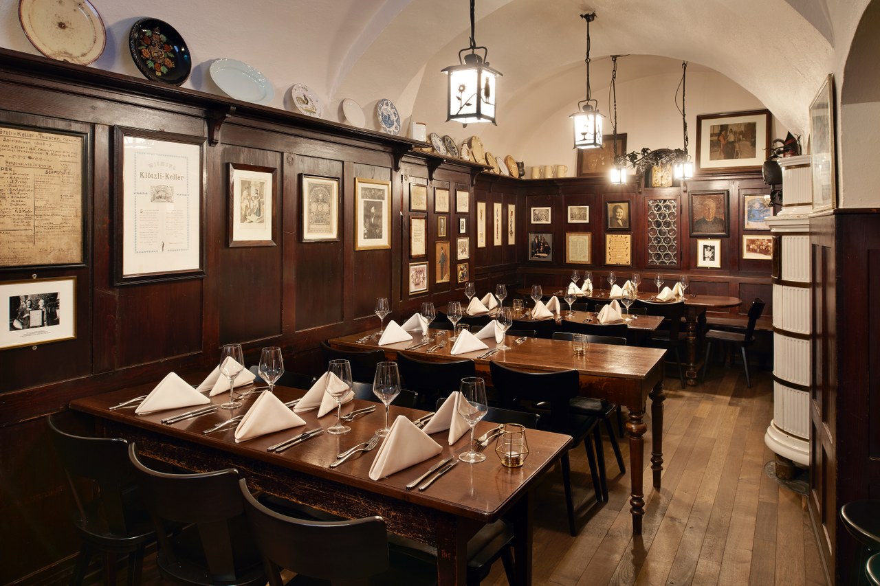 Das Foto zeigt das Restaurant Klötzlikeller. Zu sehen sind ein paar Tische in einem mittelgrossen, mit Holz getäfertem Raum. Die Decke überspannt mehre Bögen aus altem Mauerwerk.