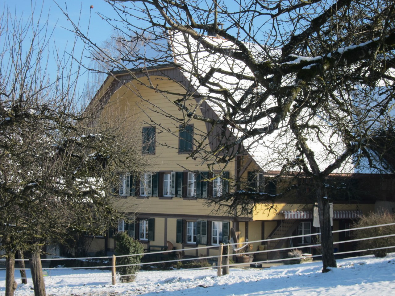 Das Foto zeigt den Biobetrieb König. Zu sehen ist ein stattliches Bauernhaus mit grossem Satteldach vor eine verschneiten Wiese