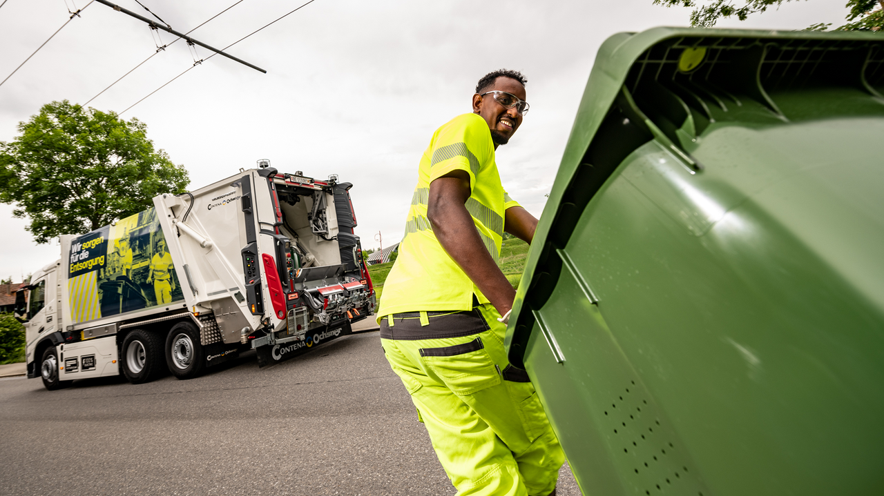 Mitarbeitender zieht Grüngut-Container richtig Kehrichtwagen