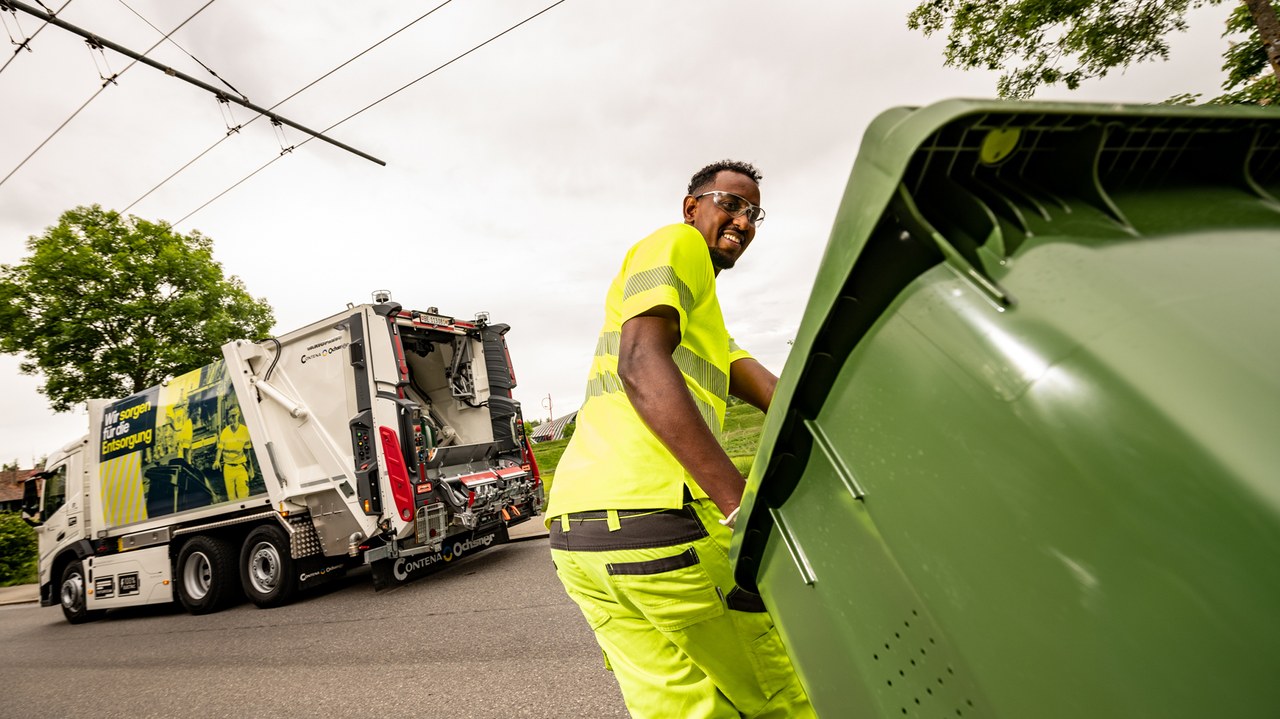 Ein Mitarbeitender bringt einen Grüngut-Container zum Kehrichtfahrzeug