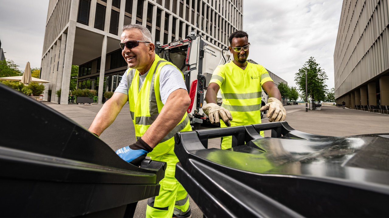 Zwei Mitarbeitende ziehen zwei Container zum Kehrichtlastwagen