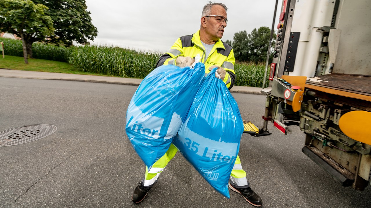 Mitarbeitender hievt zwei Kehrichtsäcke in den Kehrichtlastwagen.