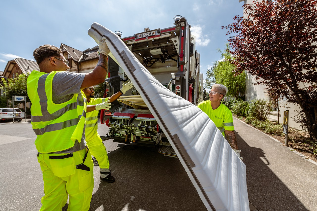 Drei Mitarbeitende laden eine Matratze in den Kehrichtwagen.