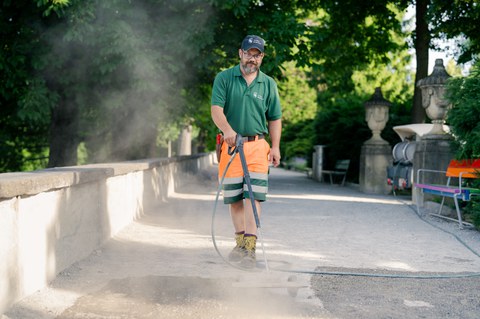 Mitarbeiter von Stadtgrün reinigt einen Parkweg mit dem Hochdruckreiniger.