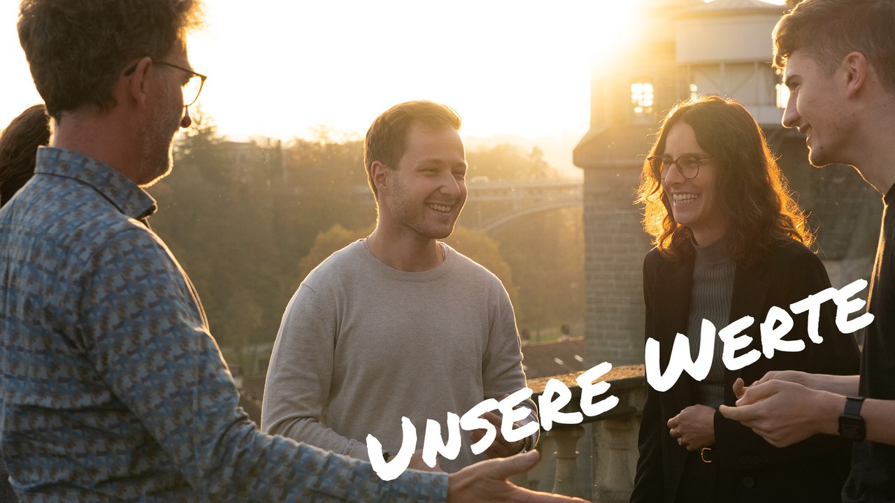Gruppe von vier Personen unterhält sich lachend im Abendlicht mit Blick auf die Kirchenfeldbrücke in Bern. Text im Bild: „Unsere Werte“.