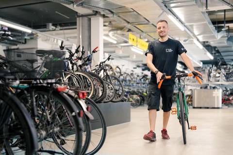 Mann schiebt ein Fahrrad durch eine grosse Velostation.