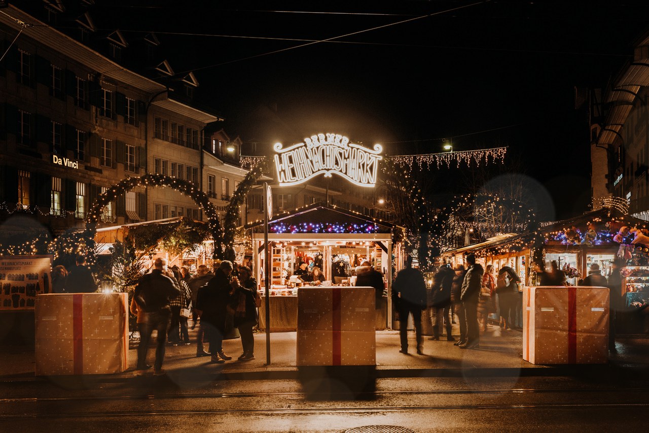 Foto: Schriftzug Weihnachtsmarkt mit Ständen und Marktbesucherinnen und Besucher