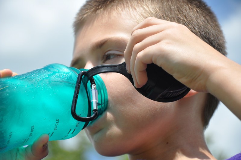 Kind trinkt aus einer Flasche Wasser.