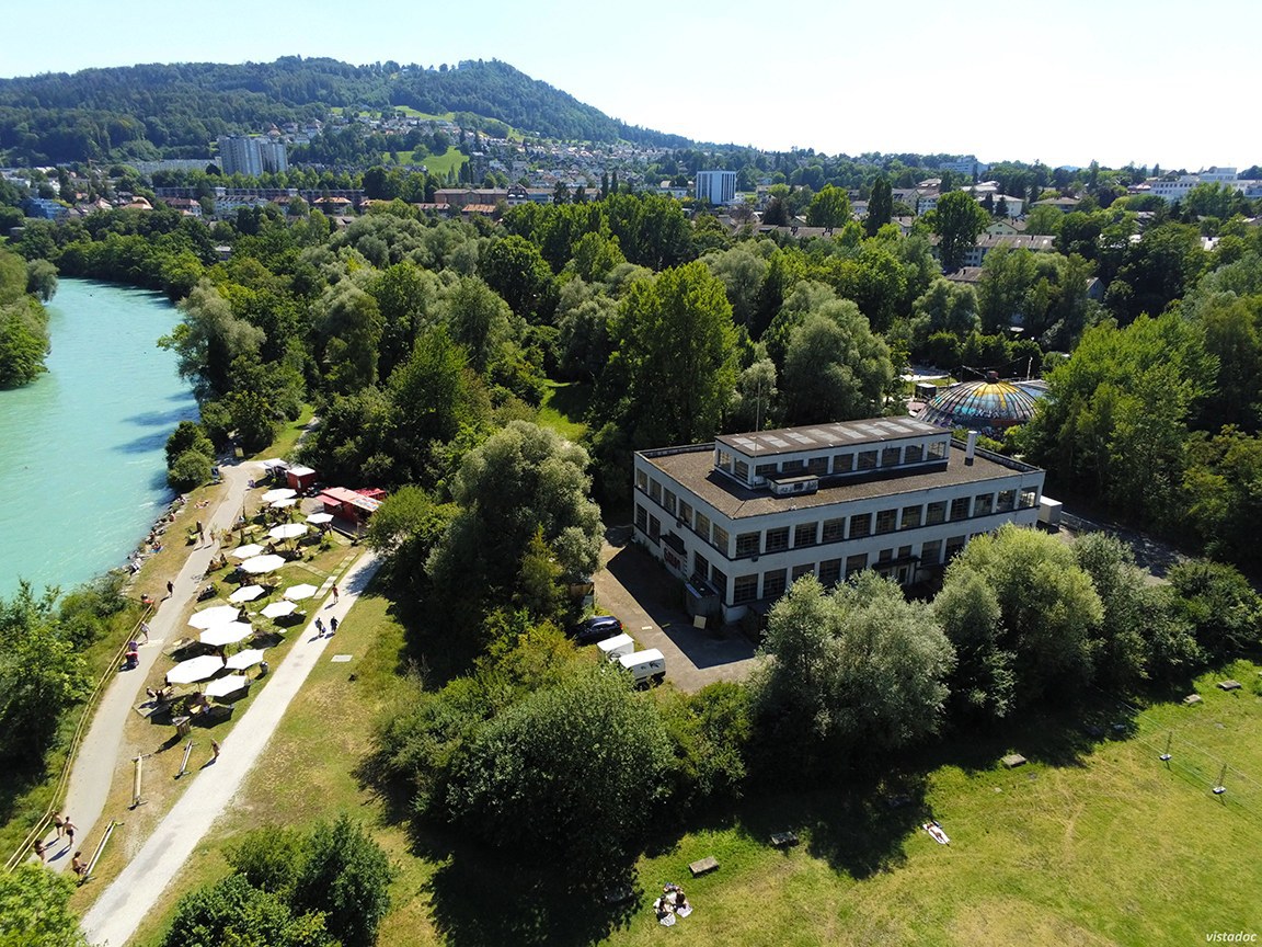 Das Foto zeigt das Werkstattgebäude von oben. Am linken Bildrand fliesst die Aare, daneben befindet sich das belebte Pup-up Aarebar. Im Hintergrund ist der Gurten zu sehen.