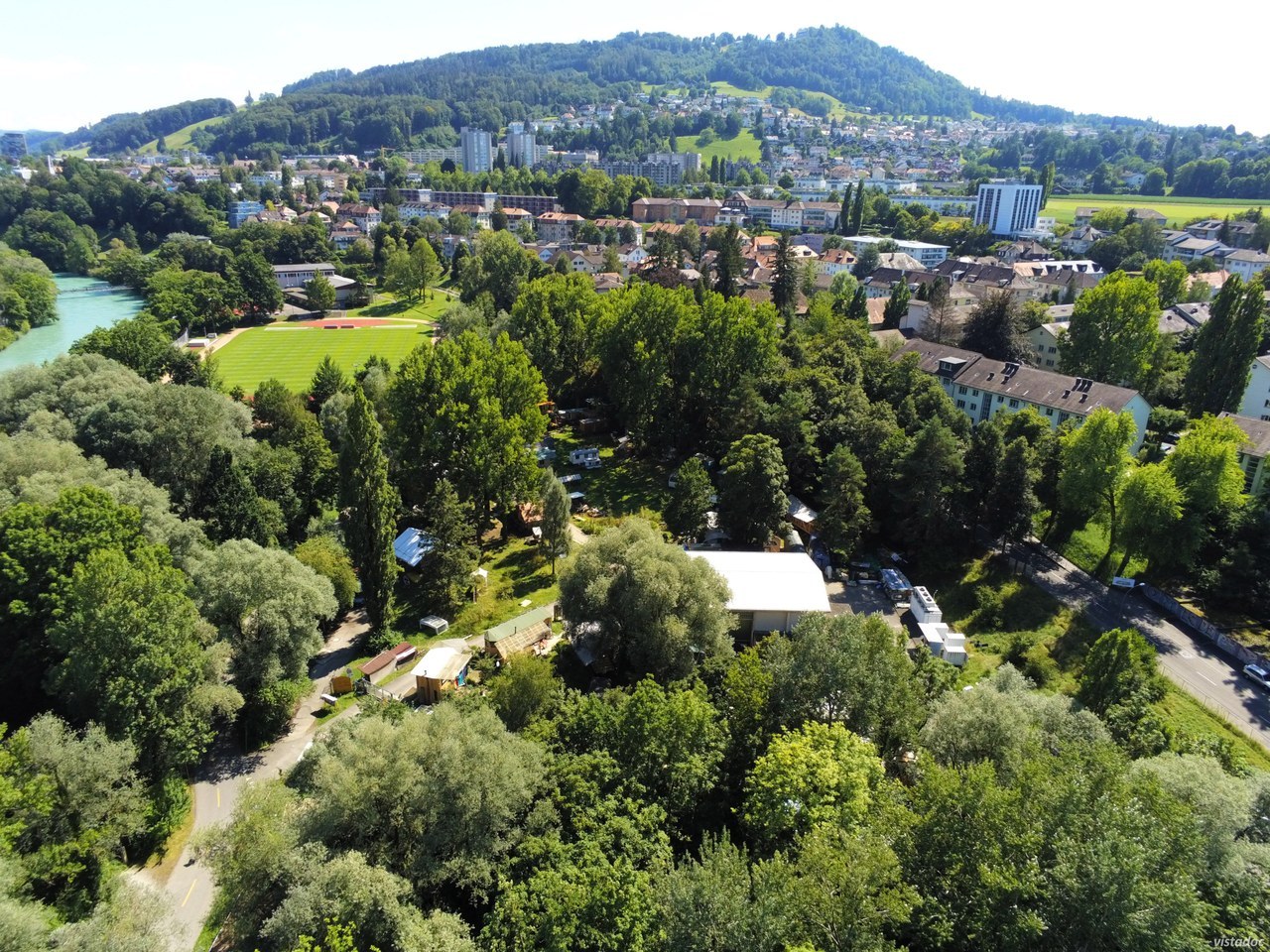 Das Foto zeigt einen Ausschnitt des Gaswerkareal, im Hintergrund bfindet sich die Sportanlage Schnönau und der Gurten. Es dominiert ein grüner Eindruck mit vielen Bäumen, am linken Rand fliesst die Aare.