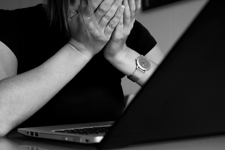 Cyberstalking: Eine Frau hält sich die Hände vors Gesicht und sitzt vor einem Laptop